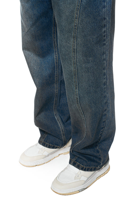 Unterer Teil der CC Core Denim Pants Tinted Indio, locker geschnitten, über weißen Sneakers. Zeigt klassischen 5-Pocket-Stil der OLAKALA®-Kollektion.