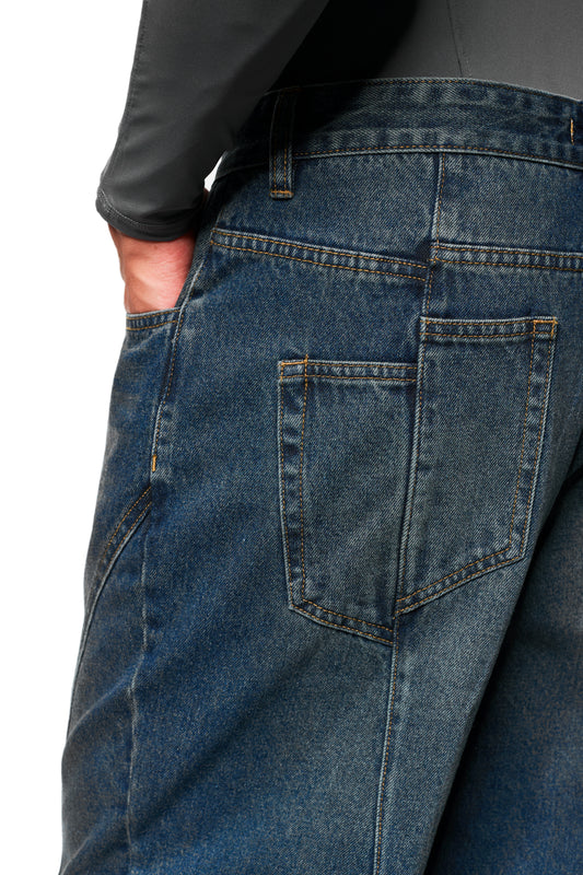 Nahaufnahme der CC Core Denim Pants Tinted Indio, zeigt die raffinierte Naht und Textur. Hand in Gesäßtasche, dunkles Oberteil sichtbar.