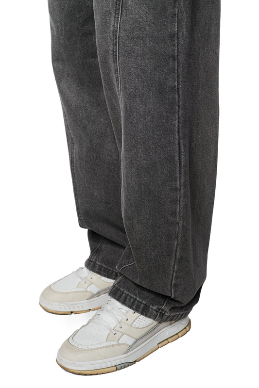 Person trägt CC Core Denim Pants in Waschgrau, moderne Jeans mit lockerem Schnitt und mittlerer Leibhöhe, kombiniert mit weißen Ledersneakern, passend zum OLAKALA-Stil.