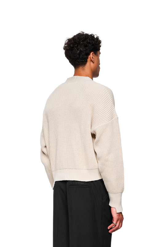 Person trägt CC Cardigan Beige mit Waffelstruktur und überschnittenen Schultern, kombiniert mit schwarzen Hosen. Oversized, cropped Design mit Metall-Pin, unisex.