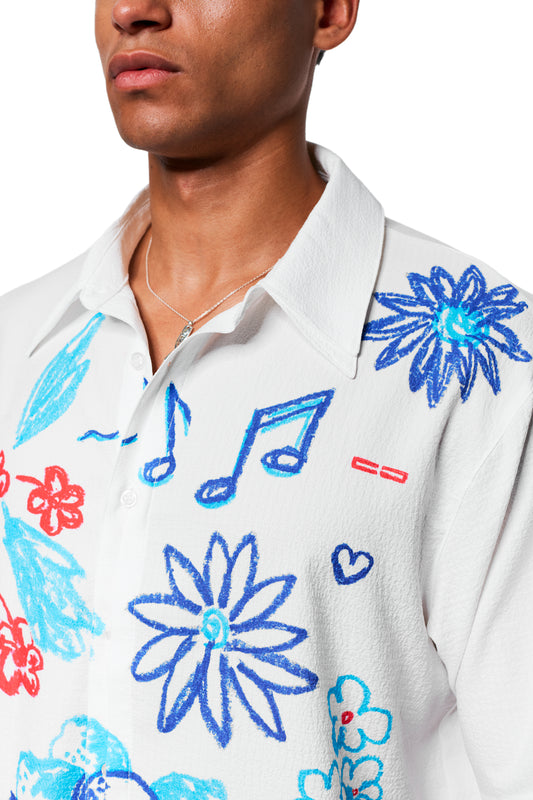 Person trägt das Crayon Summer Shirt Graphic, ein weißes Hemd mit blauen und roten Sketch-Grafiken, kubanischem Kragen, silberner Kette, perfekt für heiße Sommertage.