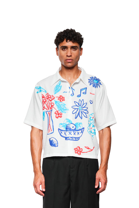 Person trägt das Crayon Summer Shirt Graphic mit handgezeichneten roten und blauen Skizzen, kubanischem Kragen und lockerer Passform. Perfekt für warme Tage.