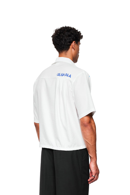 Rückansicht eines Mannes im Crayon Summer Shirt Graphic mit kubanischem Kragen und blauer Stickerei, kombiniert mit schwarzen Hosen.