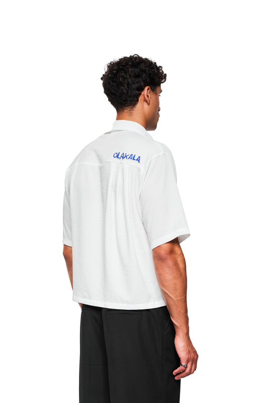 Rückansicht des Crayon Summer Shirt Heart mit handgeschriebenem „QLAKALA“-Logo auf dem Rücken, kreppartiger Textur und kubanischem Kragen, getragen von einem männlichen Modell.