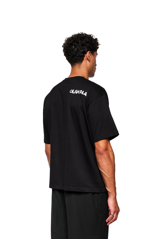 Rückansicht eines jungen Mannes im Crayon T-Shirt Oversized Black von OLAKALA, mit OLAKALA Schriftzug am Rücken, lockerer Schnitt, unisex Design.