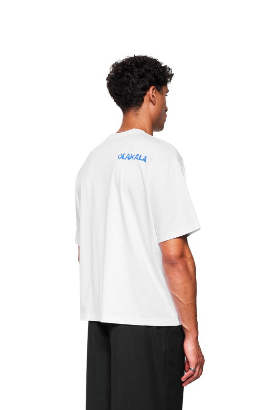Mann von hinten in lockerem Crayon T-Shirt Oversized White mit blauem OIAKALA-Schriftzug am Rücken, kombiniert mit gerade geschnittenen schwarzen Hosen.