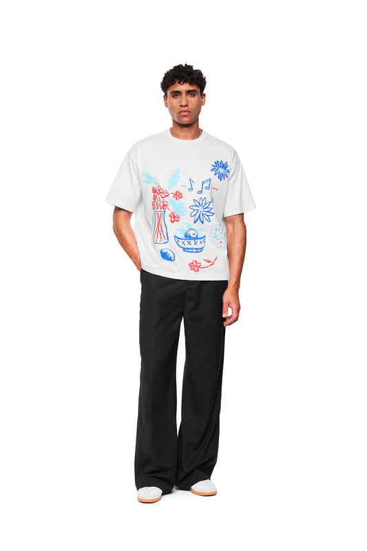 Modell trägt das Crayon T-Shirt Oversized White mit handgezeichneten Skizzen vorne, kombiniert mit weiten schwarzen Hosen und weißen Sneakers.