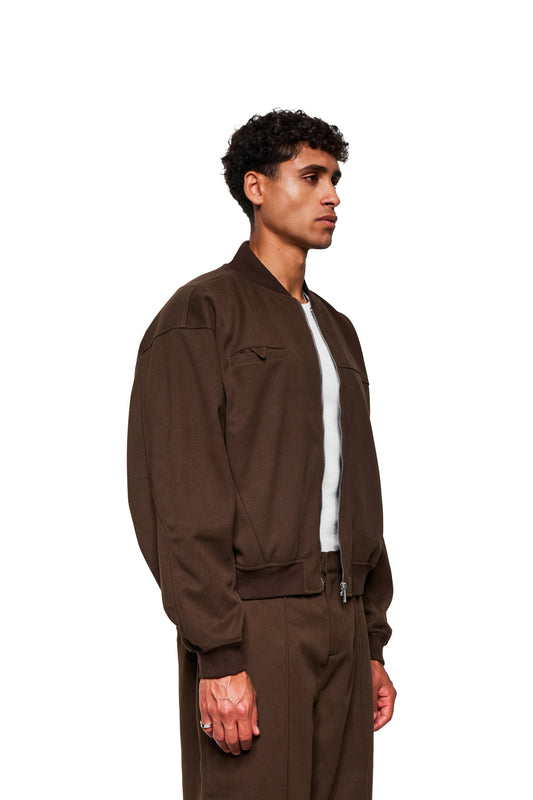 Young man in profile wearing the Exquisite Bomber Jacket Brown with ribbed stand-up collar and embroidered OLAKALA icon, showing loose, cropped fit.