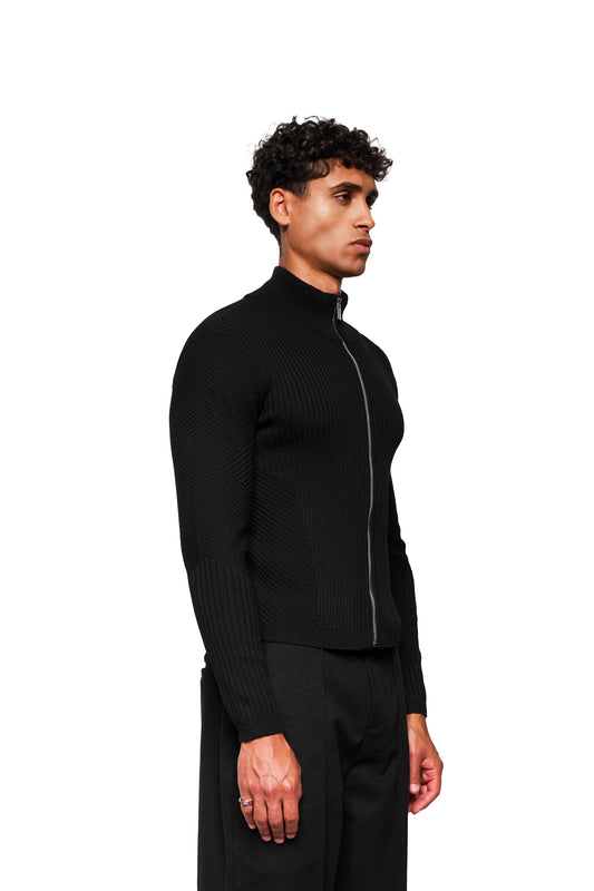 Young man in OLAKALA Exquisite Knit Jacket Black with anatomical knit pattern, stand-up collar and tight fit, complemented by matching black trousers.