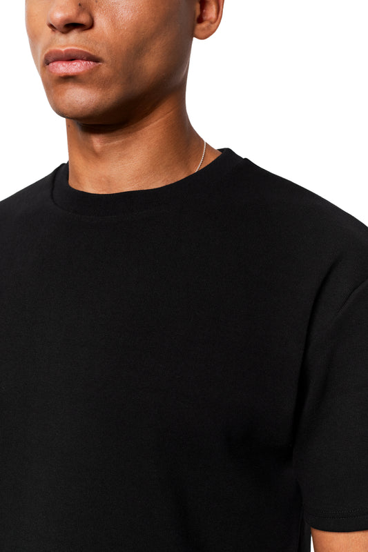 Man wears Exquisite Rib T-Shirt Black, loose fit, unisex, made of firm rib fabric, with thin chain, part of the OLAKALA® online store.