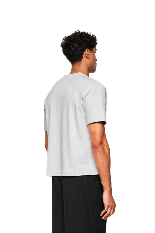 Young man in Exquisite Rib T-Shirt Gray Melange, loose fit, unisex, with loose rectangular cut and simple ring on hand against a neutral background.