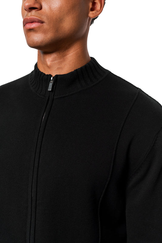 Person trägt eine schwarze Summer Knit Jacket mit asymmetrischer Front, geripptem Mock-Neck-Kragen und sichtbarem Metallreißverschluss, ideal für warme Sommerabende.