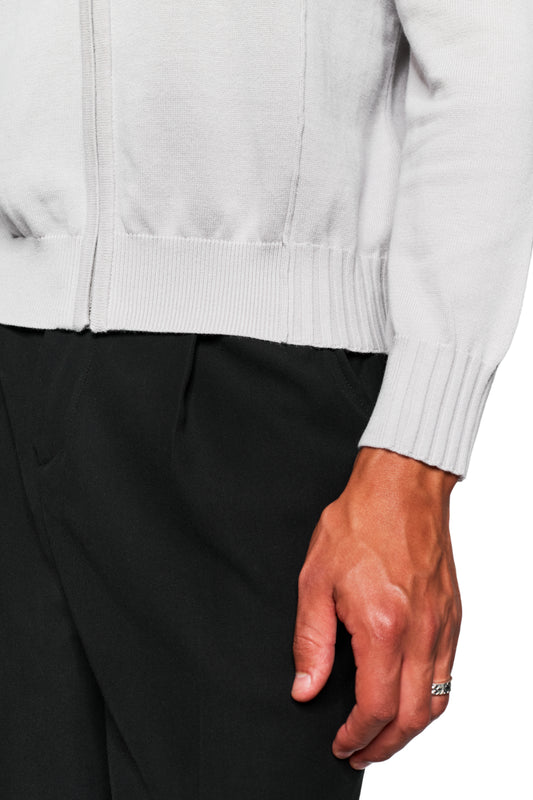 Person trägt die Summer Knit Jacket Light Gray mit asymmetrischer Vorderseite und sichtbarem Reißverschluss, kombiniert mit dunkler Hose und silbernem Ring am Finger.