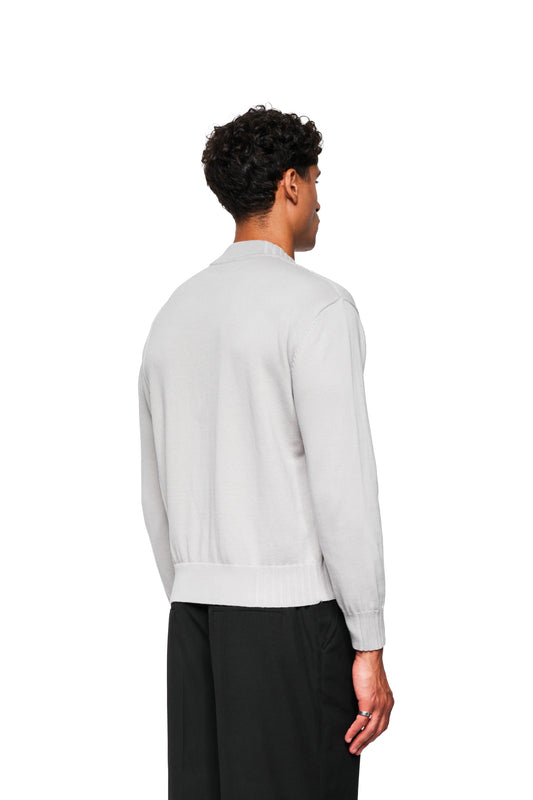 Ein Mann trägt die Summer Knit Jacket Light Gray mit asymmetrischer Vorderseite und verschiedenen Strickmustern, passende schwarze Hose, ideal für warme Sommerabende.