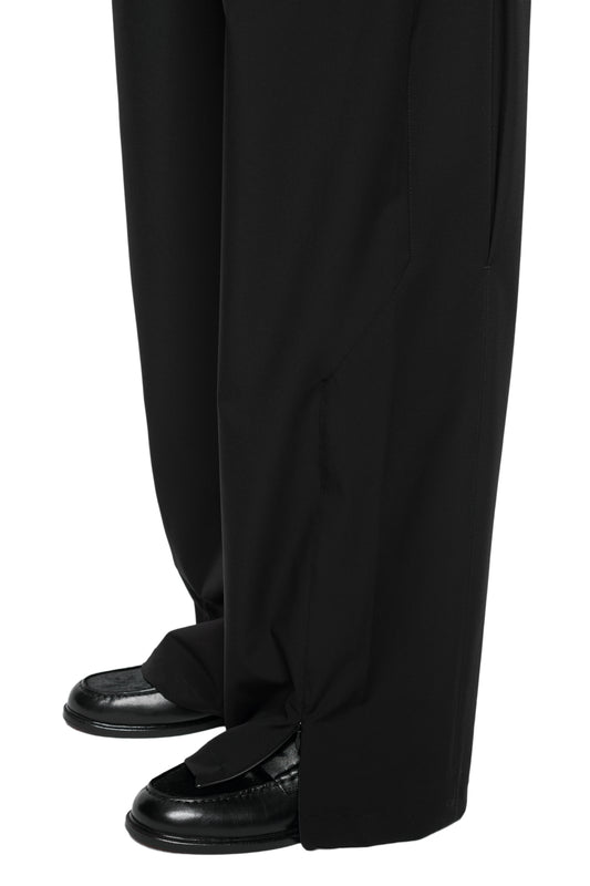 Person wears Exquisite Tech Pants Black with a loose fit, visible zipper detail at the hem and falling over shoes.