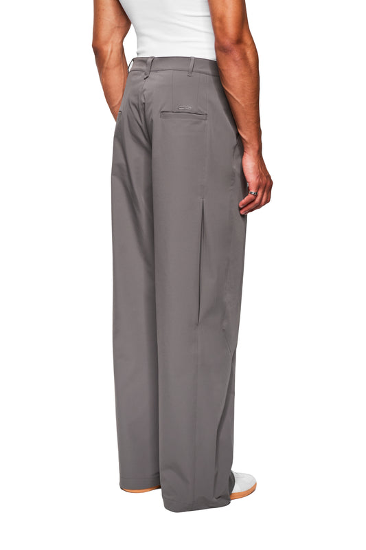 Rear view of a person in gray Exquisite Tech Pants with a loose fit, asymmetrical pocket opening and box pleat, worn with a white top and sneakers.