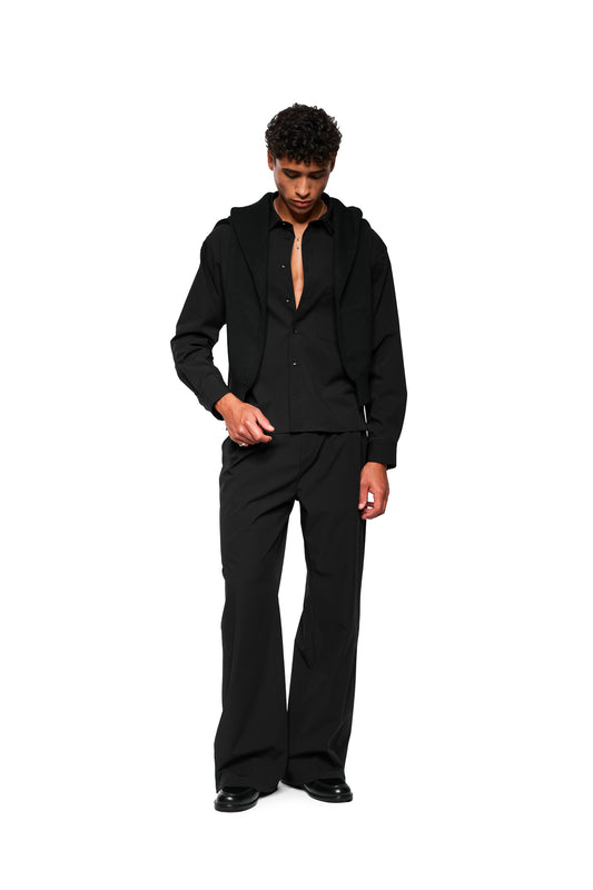 Model wears Exquisite Tech Pants Black with asymmetrical pocket opening and pleats. Robust, stretchy material for comfort. Loose cut, unisex.