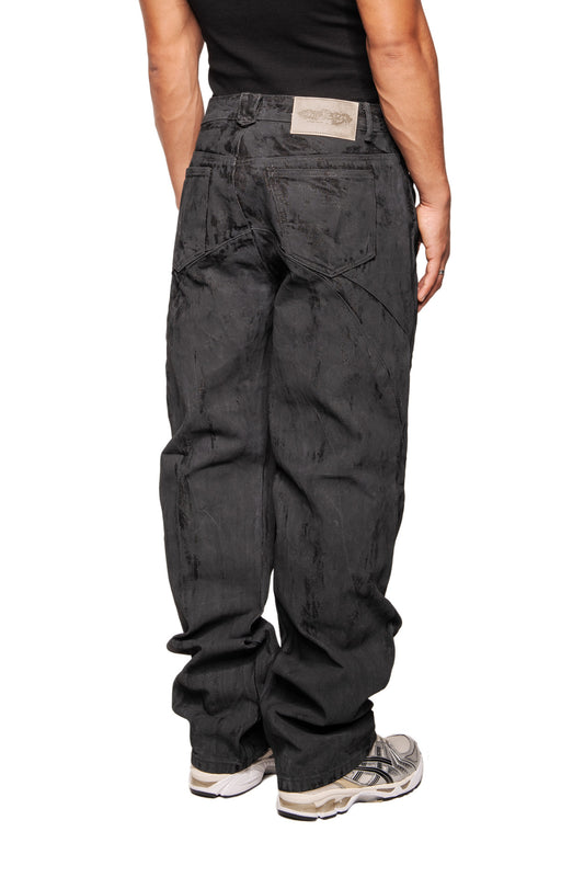 CI Coated Denim Pants Regular, loose-fitting black baggy jeans with destroyed all-over print, dividing seams, offset side seam and OLAKALA branding, worn with light-colored running shoes.