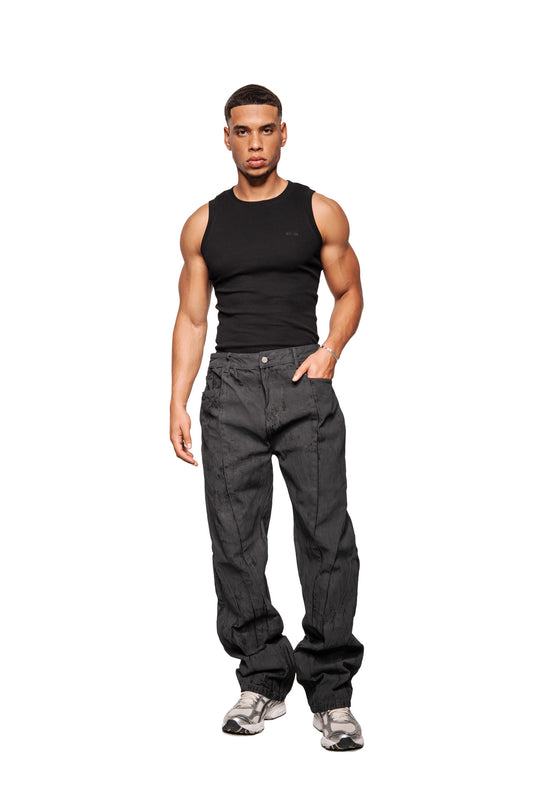 Young man in CI Coated Denim Pants Regular with visible dividing seams and 5-pocket design, matching the OLAKALA collection, looks directly into the camera.