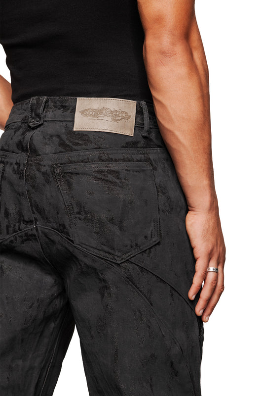Back view of CI Coated Denim Pants Regular with embossed OLAKALA leather patch, dividing seams, single back pocket and silver ring on the right middle finger.