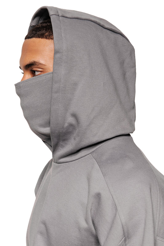 Person trägt Discreet Mask Hoodie Dark Gray mit hochgezogenem Kapuzen- und Maskenteil, zeigt oversized, cropped Fit und gesticktes OLAKALA Defect Identity Icon auf der Brust.