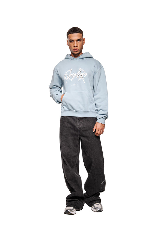 Junger Mann trägt den Fusion Hoodie Blue mit Kängurutasche und abstrakter Fusion-Grafik, kombiniert mit weiten Jeans und grauen Sneakers. Unisex, reguläre Passform.