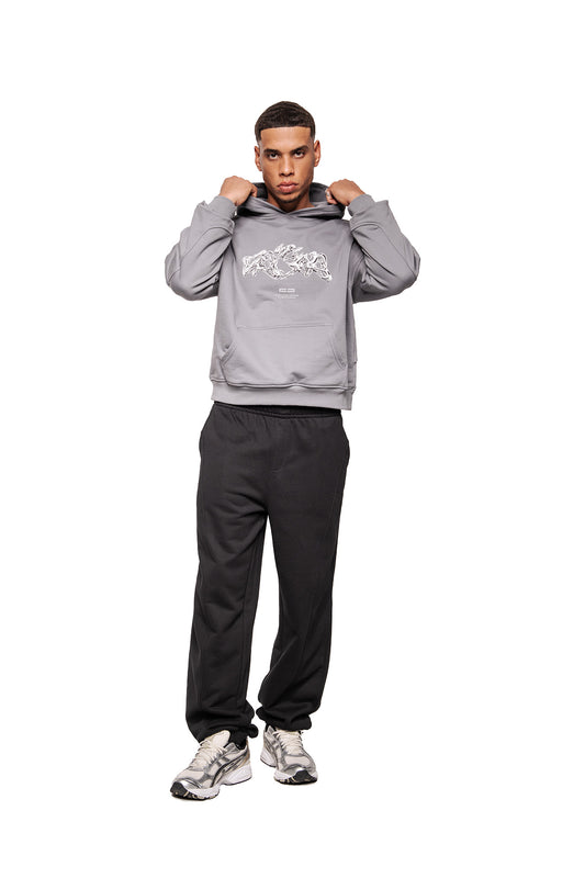 Model wears Greyzone Hoodie Dark Gray with kangaroo pocket and screen print graphic on the chest, combined with black sweatpants and gray running shoes.