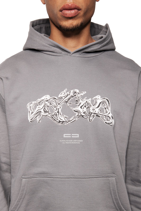 Person wears the Greyzone Hoodie Dark Gray with metallic graphic print OLAKALA © 2024 GREYZONES on the chest and kangaroo pocket, regular unisex fit.