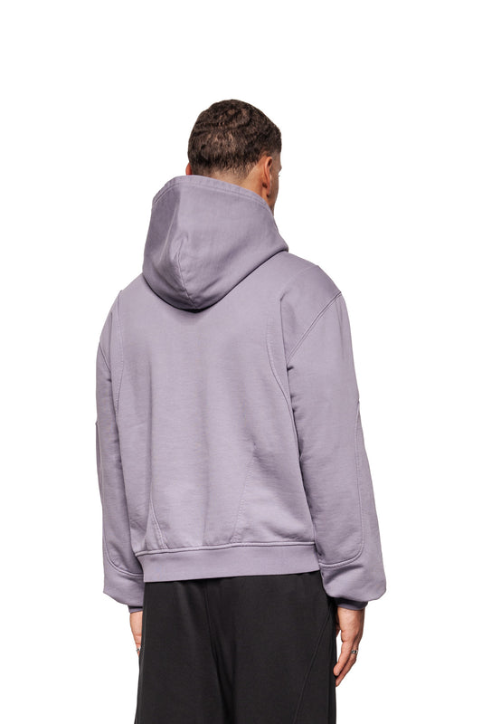Model from behind in a Greyzone Hoodie Lilac with hood and ribbed cuffs, combined with loose black pants, against a white background.