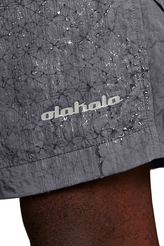 Nahaufnahme von Swim Shorts Light Gray mit reflektierendem Logo-Print und Monogramm-Effekt bei Wasserkontakt, elastischem Bund und personalisierten Kordelzug-Spitzen.