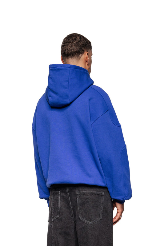 Person from behind in oversized Synergy Mask Hoodie Blue with ribbed cuffs and elastic hem, combined with faded jeans.