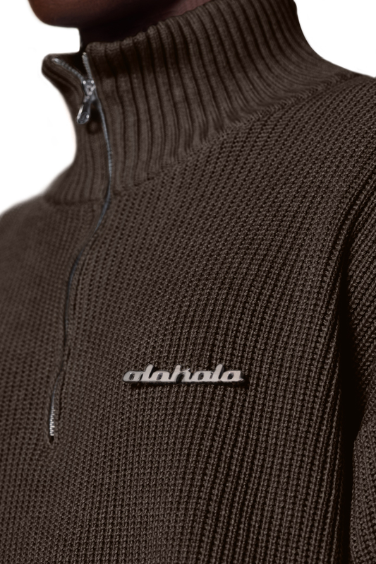 Nahaufnahme eines braunen Strickpullovers mit halbem Reißverschluss, verschiedenen Strickmustern, überschnittenen Schultern und versetztem Saum, Teil der OLAKALA-Kollektion.