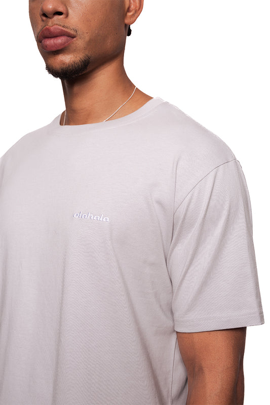 Mann trägt NC T-Shirt Grau Regular mit schwarzem OLA KALA Logo auf der Brust, dünner Kette, schlichter Stil, Teil des OLAKALA® Sortiments.