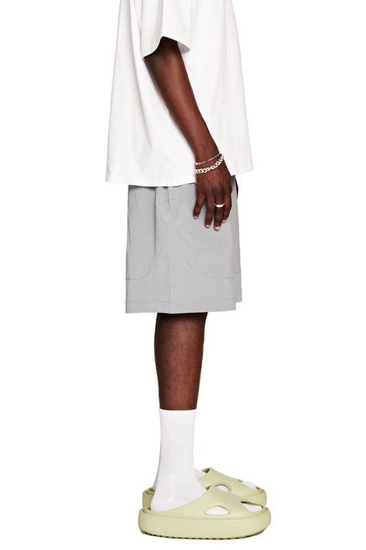 Man wears Terra Track shorts with zippered trouser pockets and drawstring, visibly breathable and unisex, made of Italian fabric, matching the OLAKALA store style.