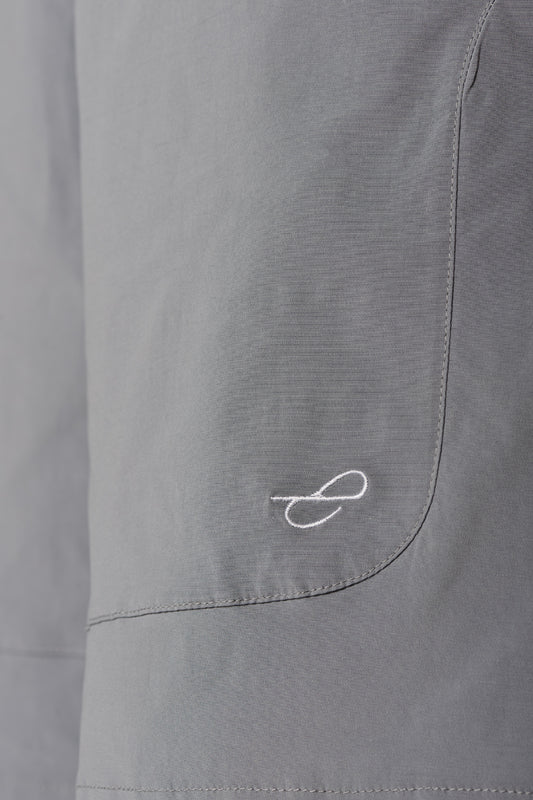 Terra Track shorts with close-up of a pocket and visible dividing seam, zipper pocket and embroidered E logo on gray linen fabric, unisex design.