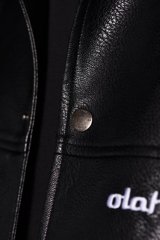 Close-up of a press stud of the CC Leather Jacket Black OLD made of vegan leather with zipper and embroidered logo by OLAKALA.