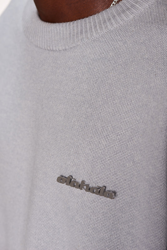 Nahaufnahme des CC Knit Sweater Gray mit überschnittenen Schultern und OLAKALA Metall-Pin, präsentiert in unisex oversized Passform.