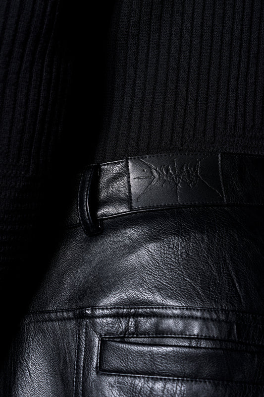 Close-up of the Discreet Leather Pants with embossed OLA KALA patch on the waistband, side airflow slits and front pockets.