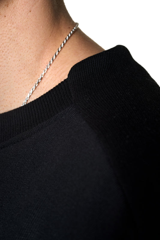 Person wears the Defect ID Sweater Black with ribbed cuffs and a special neck finish. Seam details and an oversized fit complete the unisex design.