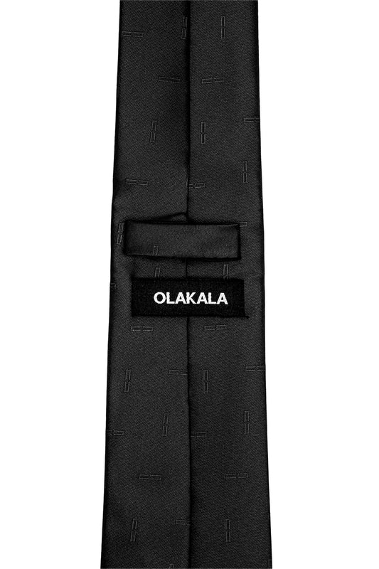 The back of the black monogram tie with OLAKALA label on the loop shows a subtle pattern of small, raised horizontal stripes.