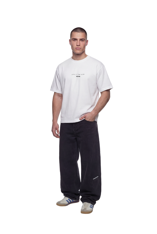 Modell trägt das Heart T-Shirt White mit Blindenschrift-Print auf der Brust, kombiniert mit weiten schwarzen Hosen und weißen Sneakers mit blauen Streifen.