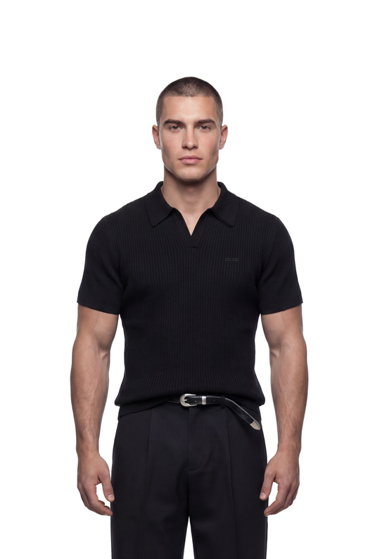 Junger Mann trägt ein CC Core Rib Knit Polo Black mit gerippter Oberfläche, moderner Silhouette und knopflosem Design, kombiniert mit schwarzen Hosen und Gürtel.