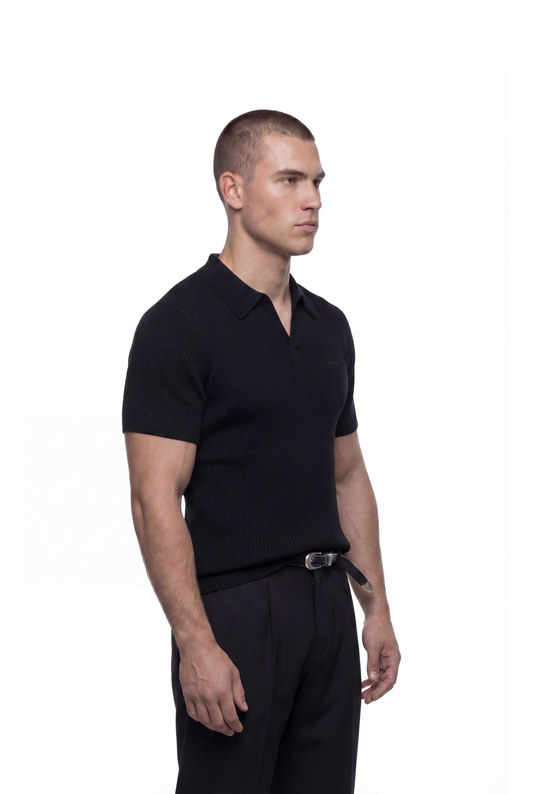 Junger Mann in CC Core Rib Knit Polo Black mit moderner, boxy Silhouette und knopflose Knopfleiste, vermittelt minimalistischen Stil vor weißem Hintergrund.