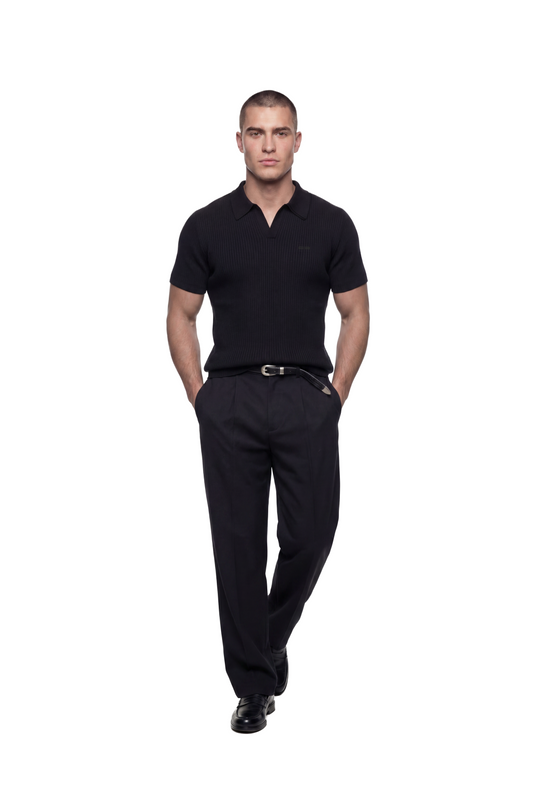 Junger Mann trägt das CC Core Rib Knit Polo Black mit knopflosem Kragen, modernem Schnitt und strukturierter Oberfläche, stehend vor weißem Hintergrund.