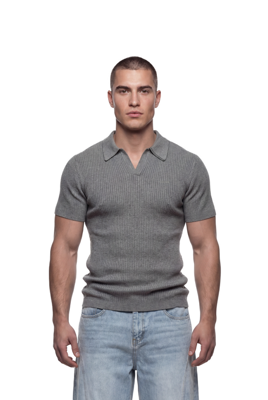 Junger Mann trägt CC Core Rib Knit Polo Gray mit gerippter Struktur und boxiger Silhouette, kombiniert mit hellblauen Jeans, vor schlichtem Hintergrund.