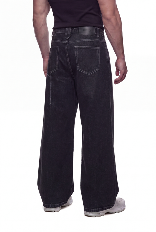 Person trägt CC Core Denim Pants Loose Black, weite schwarze Jeans mit markanten Nähten und 5-Pocket-Stil, kombiniert mit weißen Sneakers, im OLAKALA Onlineshop-Stil.