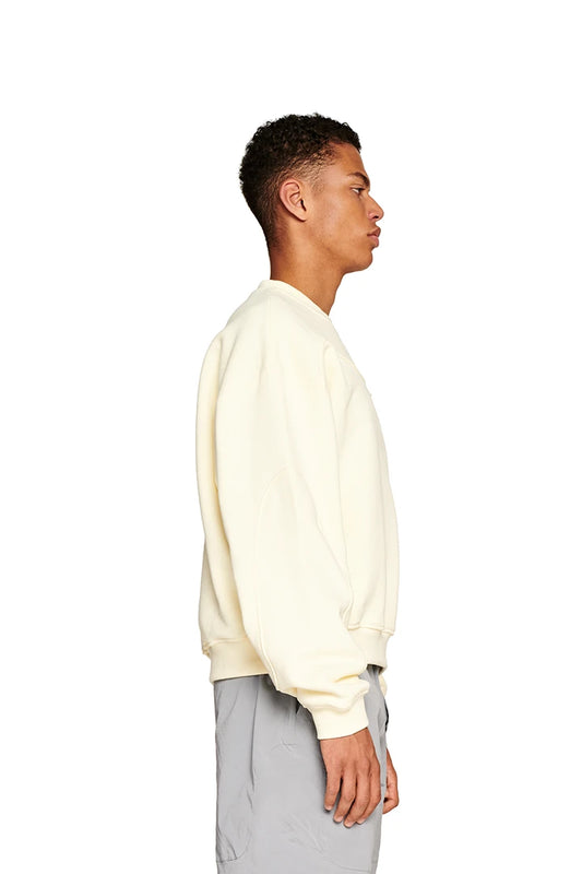 Man wearing oversized Elysium Sweater Butter with ribbed collar and Elysium logo on the chest, presented on a white background.