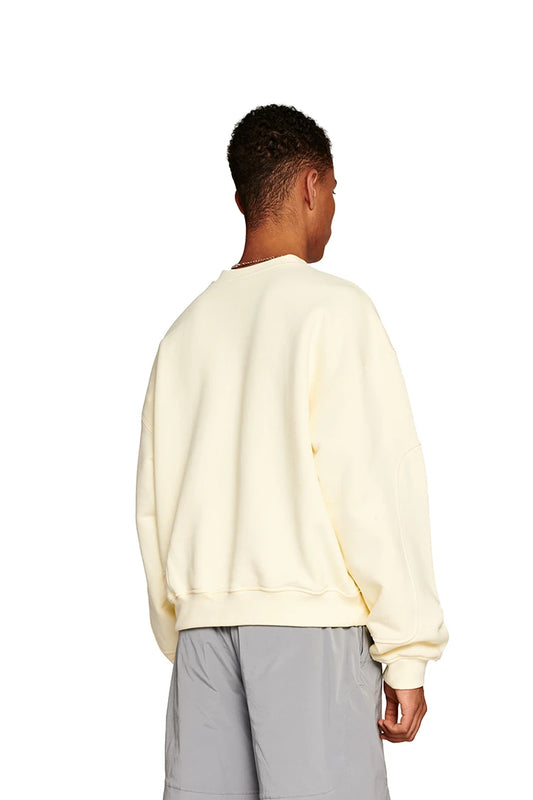 Man wears Elysium Sweater Butter with ribbed collar, cuffs and dividing seams; oversized unisex fit with Elysium logo on the chest at OLAKALA Onlineshop.