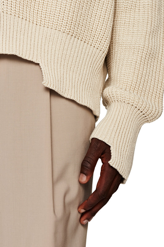 Nahaufnahme einer Hand, die den CC Cardigan Beige mit V-Ausschnitt und versetztem Saum präsentiert, passend zur oversized, unisex Mode von OLAKALA.