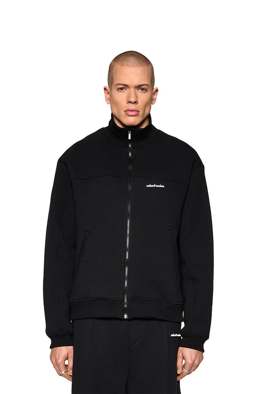 A man wears the Substance Sweatjacket Black with OLAKALA silicone patch, zipped pockets and ribbed collar for a casual look.
